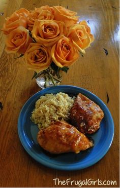 a blue plate topped with meat and rice next to orange roses on a wooden table