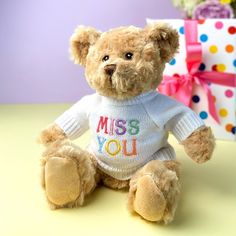 a teddy bear wearing a sweater with the words miss you on it sitting next to a gift box