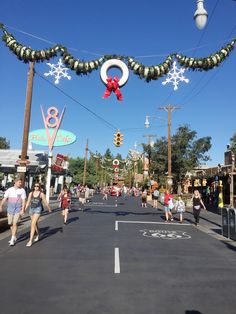 people are walking down the street in front of christmas decorations on poles and lights hanging above them