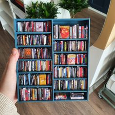 a person is holding up a book case filled with many different books and dvds in it