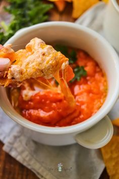 a person holding up a piece of pizza in a bowl filled with tomato sauce and cheese