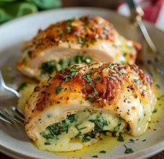 two pieces of chicken covered in cheese and spinach on a plate with a fork