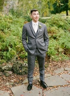 a man in a suit and tie standing on a stone walkway with trees behind him