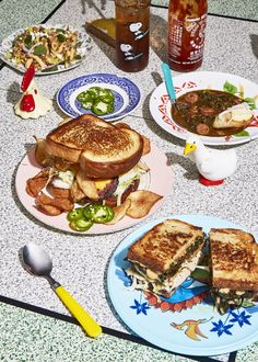 a table topped with plates filled with sandwiches and bowls of food next to cups of soup