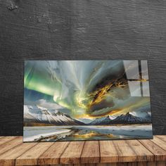 an art piece on a wooden table in front of a black wall with mountains and clouds