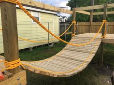 a wooden bridge with yellow rope on it in the grass next to a house and fence