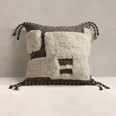 a pillow with a house on it and tassels hanging from the front, sitting on a white surface