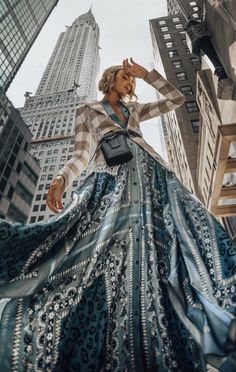 a woman standing in front of tall buildings wearing a blue and white dress with an animal print skirt