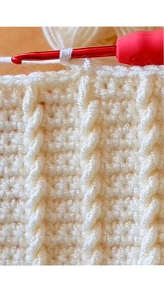 the crochet stitch is being worked on by a red handled knitting needle and yarn ball