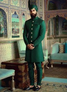 a man in a green outfit standing next to a blue couch and ottoman with an ornate wall