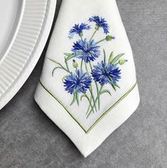 a white plate with a blue flower embroidered on it next to a tie that has flowers on it