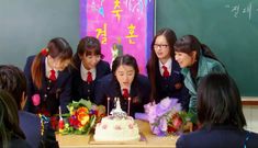 a group of girls standing around a table with a cake on it and candles in front of them