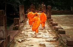 three monks in orange robes are walking down a path between stone pillars and brick structures