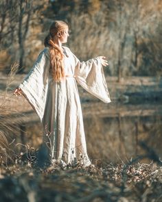 a woman dressed in white is standing by the water