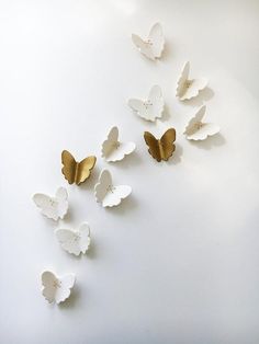 several white and gold butterflies flying in the air on a white surface with no one around them