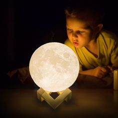 a young boy is looking at the moon lamp