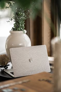 an apple laptop sitting on top of a wooden table next to a potted plant