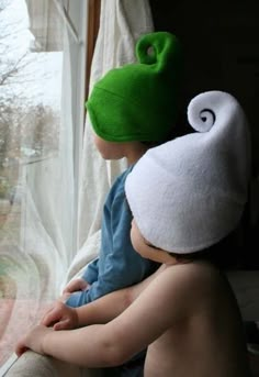 a young child wearing a green hat and sitting next to another child in front of a window