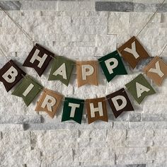 a happy birthday banner hanging on a brick wall with the words happy birthday spelled in brown and green