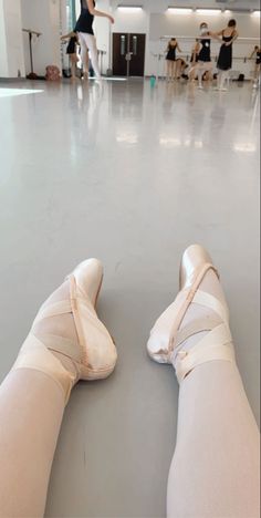 the legs and feet of a ballerina wearing ballet shoes in an empty room with other dancers