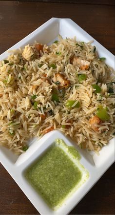 a white plate topped with rice and veggies next to a small green sauce