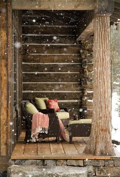 a chair sitting on top of a wooden deck under a tree covered in snow next to a log cabin