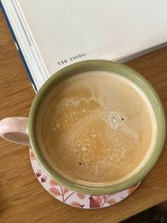 a cup of coffee sitting on top of a wooden table next to a book and pen