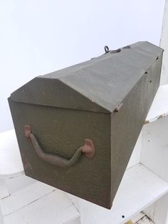 an old trunk hanging from the side of a white wall with a handle on it