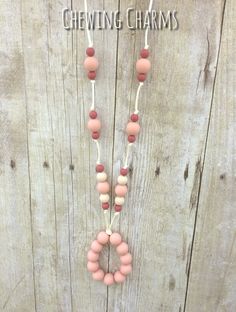 a pink and white beaded necklace hanging on a wooden wall with the words chewing charms written above it