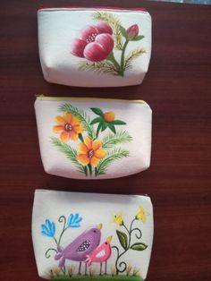 three small containers with flowers painted on them sitting on top of a wooden table next to each other