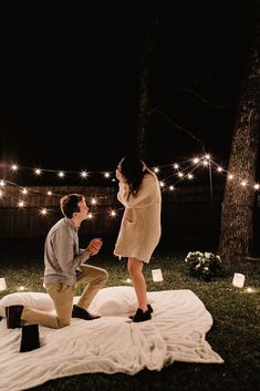 a man kneeling down next to a woman on top of a blanket