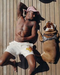 a shirtless man laying next to a dog on a wooden deck with his leg up