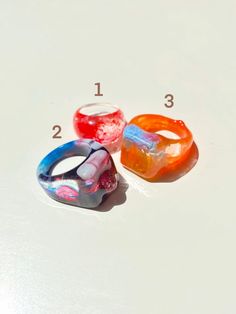 "Colorful and shiny statement rings. Each ring is one of a kind (they have different sizes). You can choose to purchase only one ring, or the three rings in the listing (Prices vary depending on the option you choose). Please select the number of the ring you want or if you would like to take all of them please click the option \"All three rings\". You will receive the exact ring/rings shown in the pictures. Ring 1 Diameter: 17 mm Ring 2 Diameter: 19 mm Ring 3 Diameter: 19 mm" Unique Clear Resin Ring, Unique Clear Resin Rings, Trendy Resin Ring Jewelry, Unique Multicolor Resin Ring, Trendy Resin Ring, Clear Resin Rings, Trendy Multicolor Plastic Rings, Trendy Multicolor Resin Rings, Multicolor Lucite Jewelry For Gift