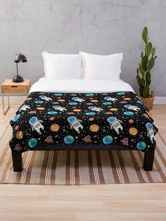 a bed with a black blanket that has an image of space shuttles and planets on it