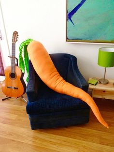 a giant carrot sitting on top of a blue chair next to a guitar and lamp