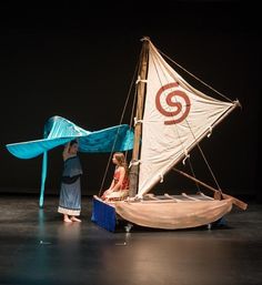 two children are playing with a model sailboat on the stage in front of them