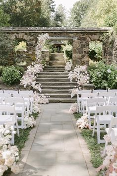 an outdoor ceremony setup with white chairs and pink flowers on the steps leading up to it