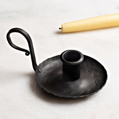 a black teapot with a yellow handle on a white surface next to a pen