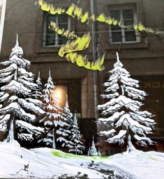 snow covered trees in front of a window with the reflection of a building behind it