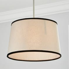 a white lamp hanging from a ceiling with a black trim around the drum light shade