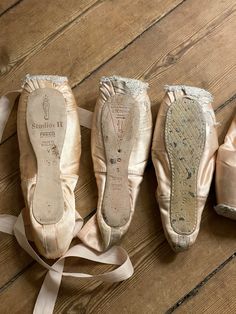 three pairs of ballet shoes are lined up on a wooden floor with ribbons around them