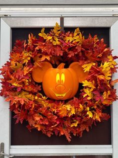 a mickey mouse pumpkin wreath on a door with fall leaves around it and a face carved into the front