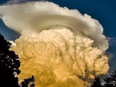 a large cloud is in the sky above some trees