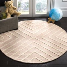 a teddy bear is sitting on the floor in front of a round rug with diagonal stripes