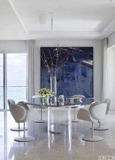 a dining room table with white chairs and a large painting on the wall behind it