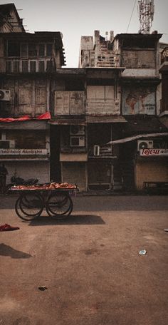 an empty street with people walking around and buildings in the background, one person pushing a cart full of food