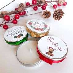 three small tins with christmas themed labels on them next to pine cones and berries