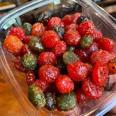 a plastic container filled with strawberries on top of a wooden table next to a person's hand