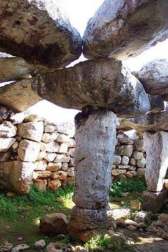 an old stone structure in the middle of a field with grass and rocks around it