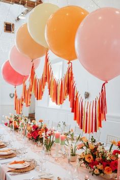 balloons and streamers are hanging from the ceiling above a long table with place settings